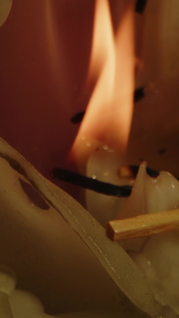 Smukt vertikalt makrobillede af orange flammer, der brænder i slow motion på en bunke voks fra et smeltet stearinlys.