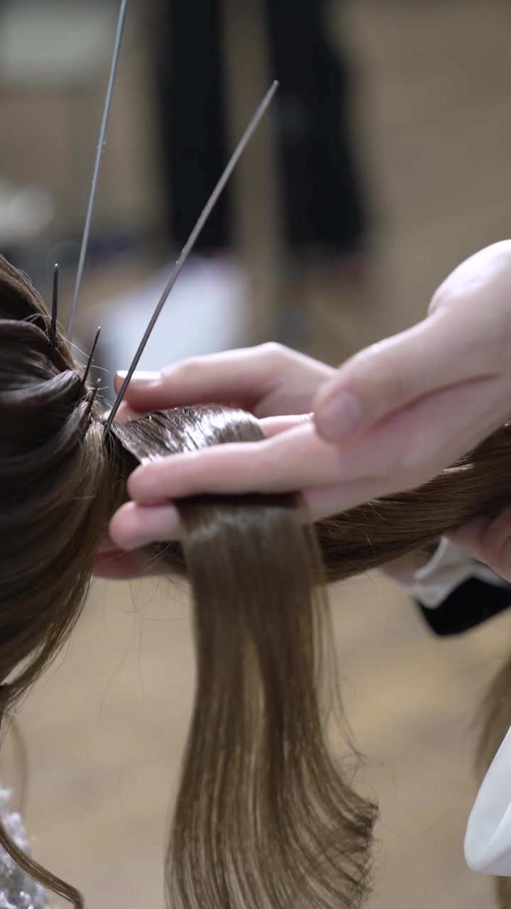 Questo mostra una persona che acconcia i capelli per un evento formale. Lo stilista utilizza strumenti per creare un look specifico. L'attenzione è sui dettagli dei capelli e sulle tecniche utilizzate