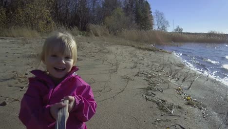 cute and happy caucasian girl, three years old, talking and playing with stick at beach in autumn