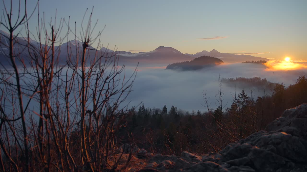 Bled, Slovenia kuvattuna auringonnousun aikaan luonnossa, jossa sumun peittämät vuoret ja maisemat kylpevät kultaisen tunnin sävyissä. Kuvaus on tehty dynaamisella liikkeellä kameralla gimbalin avulla