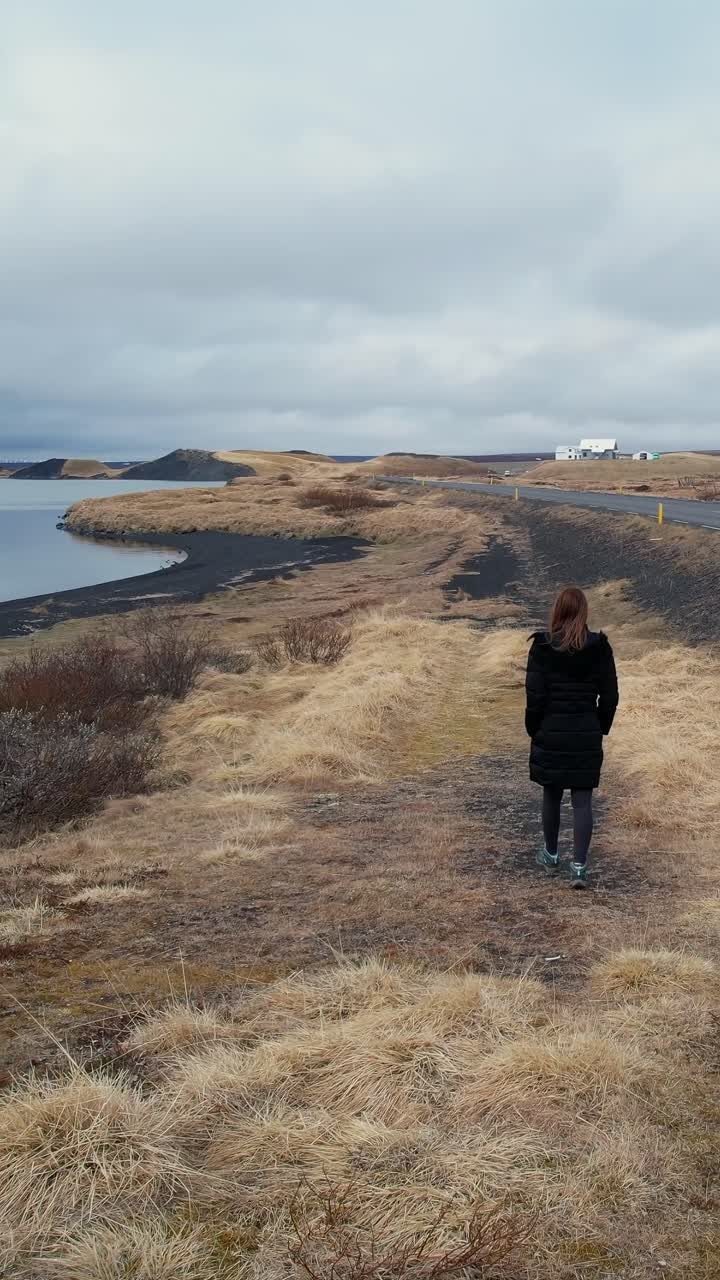 woman walking along a path on a lake shore in a moody icelandic landscape