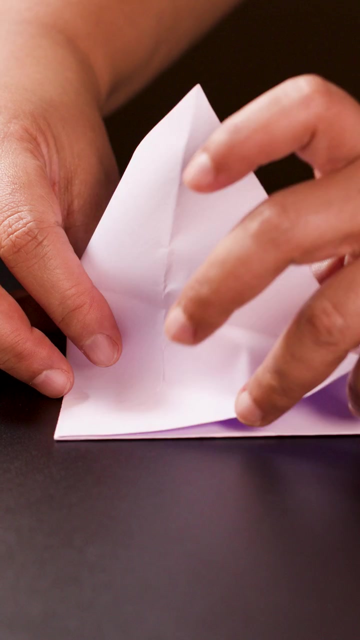 Adult hands carefully fold white paper into an origami ship under soft, even lighting