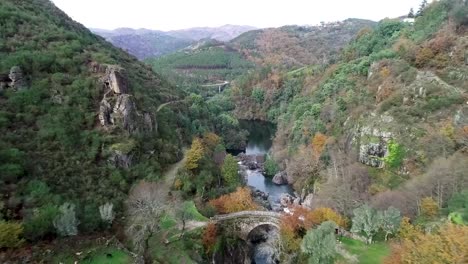 vista aérea, cañón del río rabagao, colorido follaje otoñal y puente misarela, antiguo arco de piedra en el parque nacional pedena-geres, portugal, tiro con drones