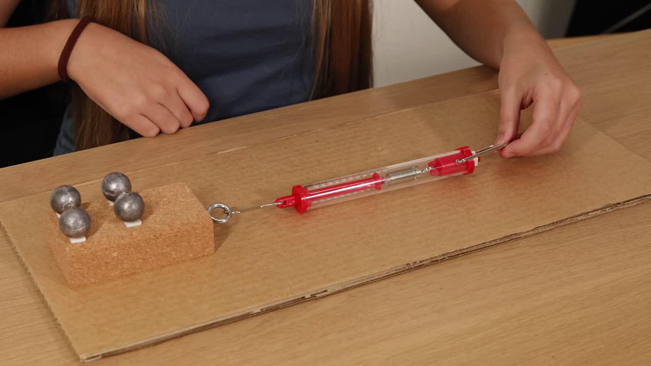 A person uses a spring scale to measure frictional force on a weighted block sliding over cardboard