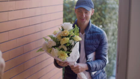 woman opening door, receiving bouquet of flowers from courier and signing the clipboard