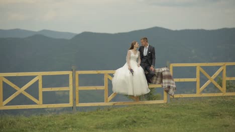 romantic wedding couple posing on a fence in the mountains