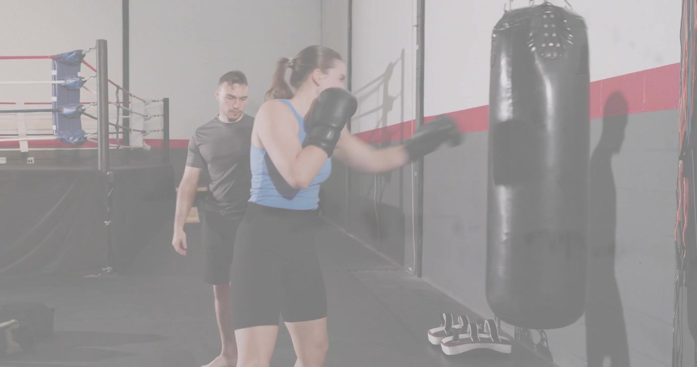 Atleta donna che si muove e sferra combinazioni sul sacco da boxe per l'allenamento, mentre l'allenatore la segue.