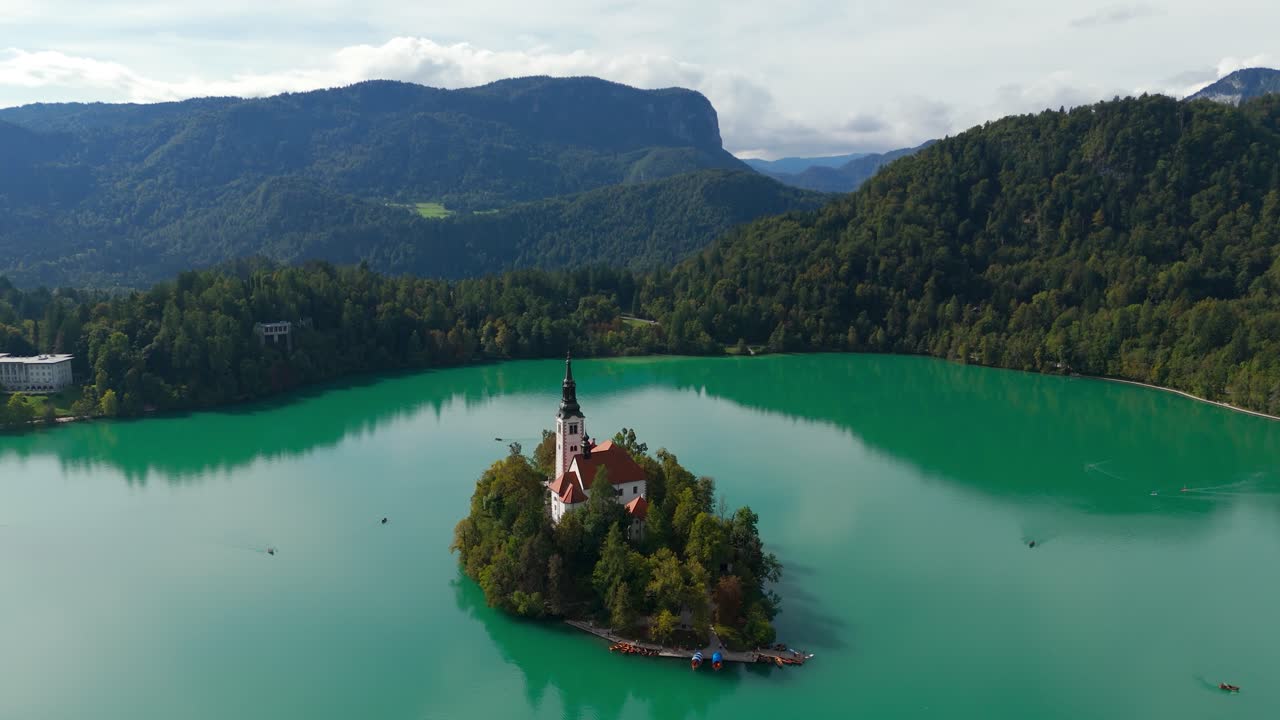 Iconic and historic pletna boats beached on shore of Bled island in lake, aerial