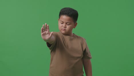 asian boy showing stop hand while standing on green screen in the studio