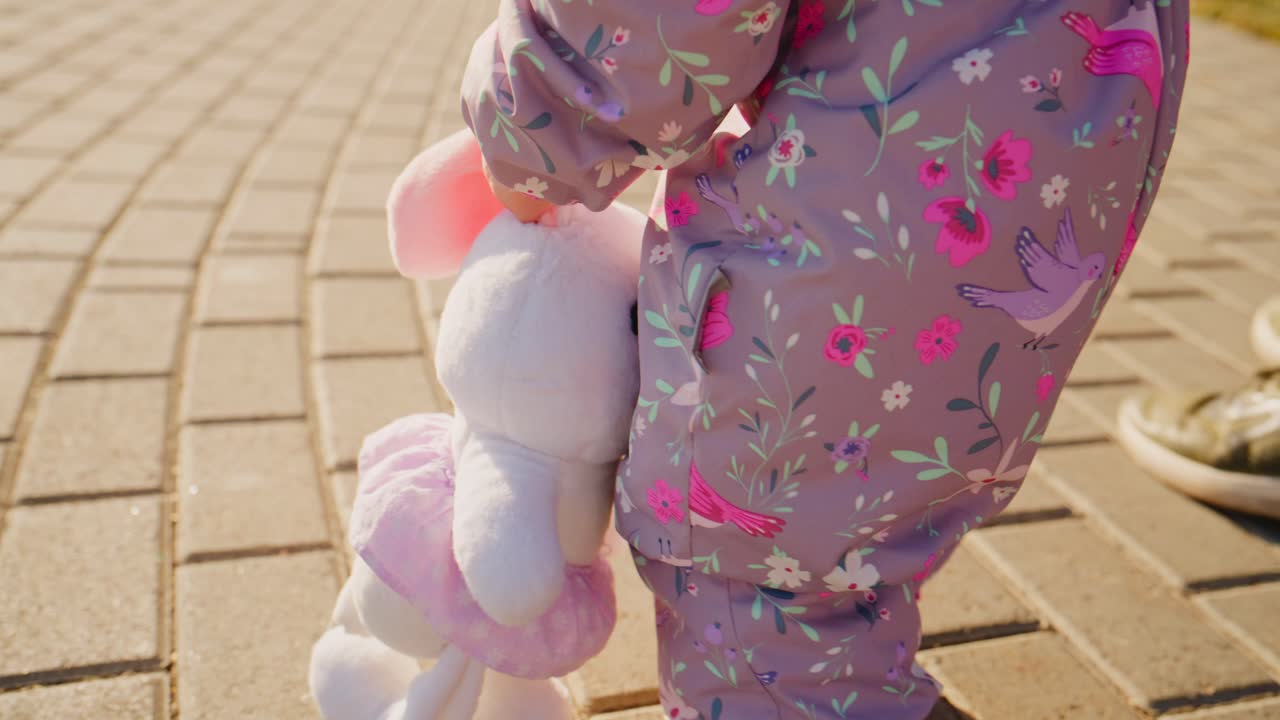 A Child's Joyful Stroll Holding a Plush Toy While Walking on a Sunlit Paved Pathway with an Adult, Capturing Moments of Innocence and Togetherness