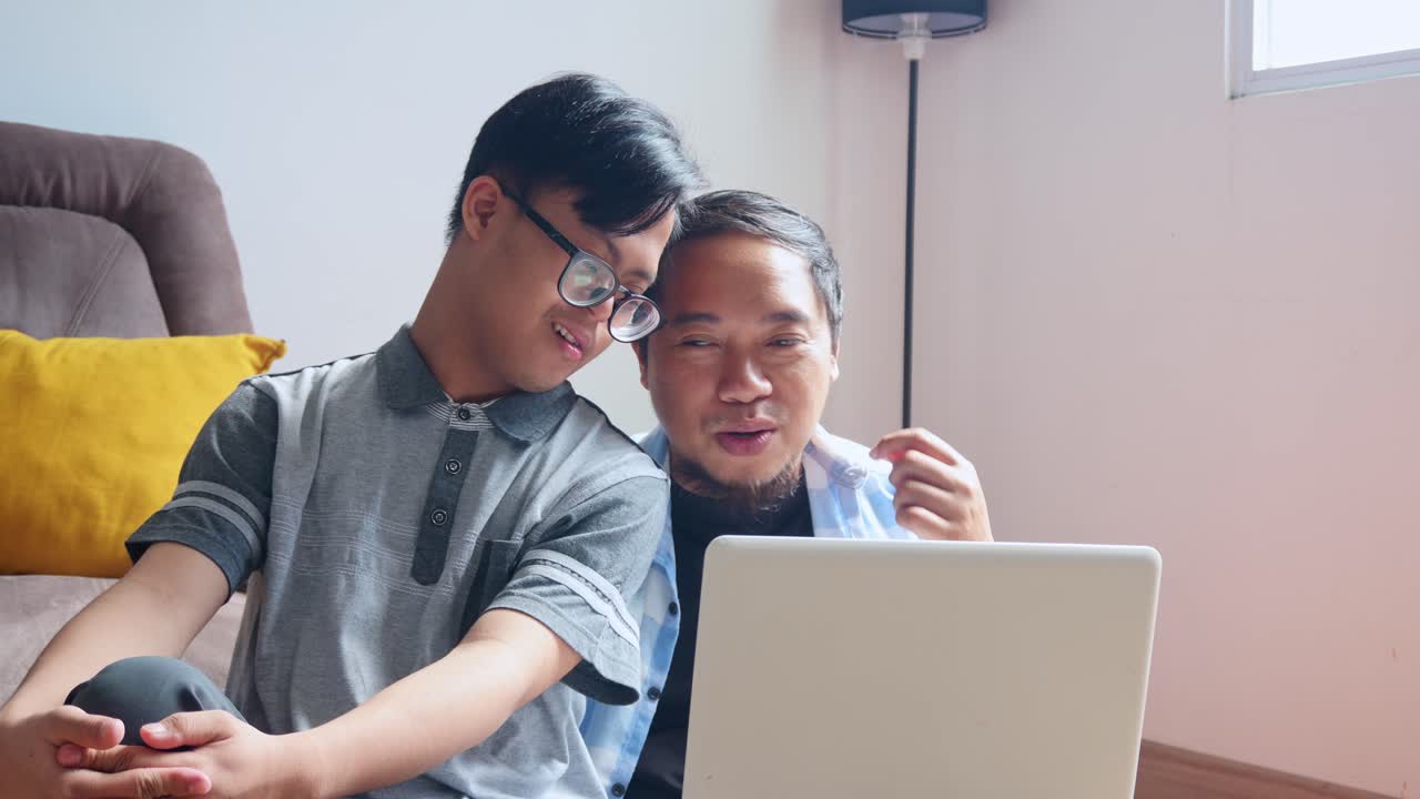 Loving father helping son with Down syndrome learn new skills using laptop at home