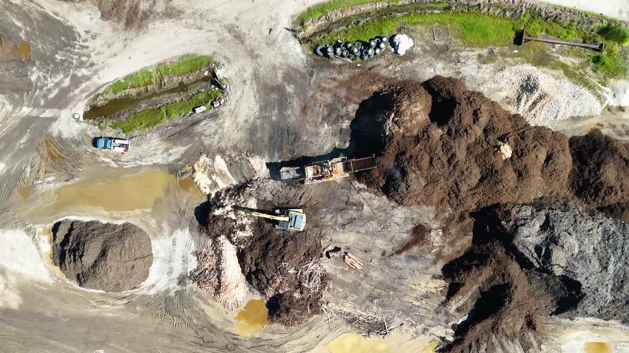 Drone footage captures machinery processing soil and mulch in an open field under bright daylight