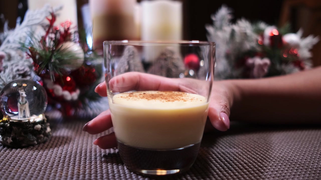 Una mano femminile che si allunga verso un bicchiere di eggnog natalizio con cannella aggiunta
