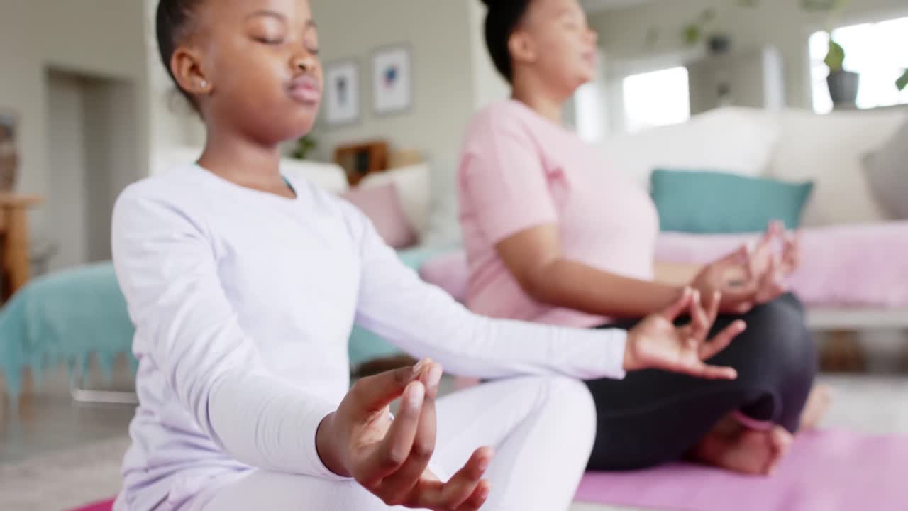 madre e hija afroamericanas felices y inalteradas haciendo meditación de yoga en casa, en cámara lenta