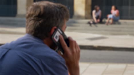 defocused shot of man talking on phone whilst sitting on street in oxford 02