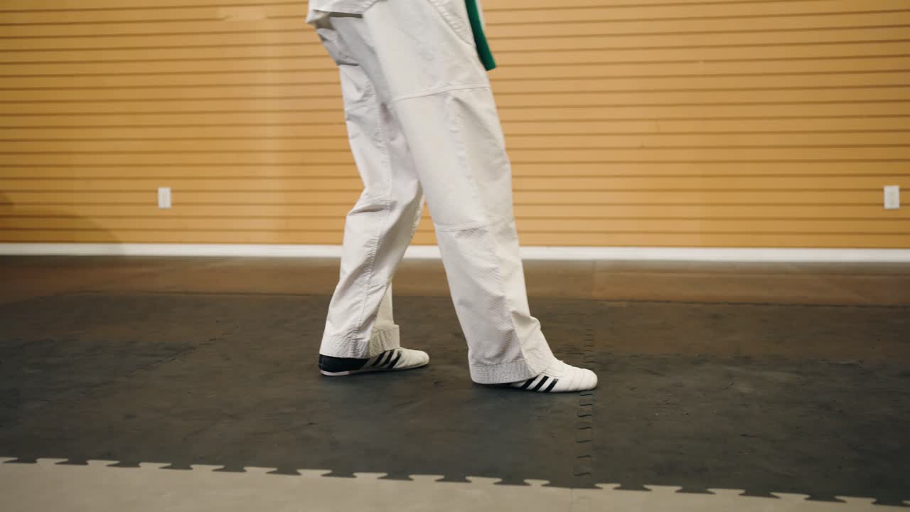 un maestro de artes marciales de cinturón negro kung fu karate taekwondo hace movimiento de pies de combate de ida y vuelta dentro de un estudio de entrenamiento de gimnasio mientras lleva un traje blanco de gi dobok