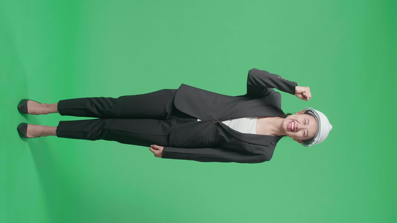 Full Body Of Happy Asian Female Engineer With Safety Helmet Celebrating While Standing On Green Screen In The Studio