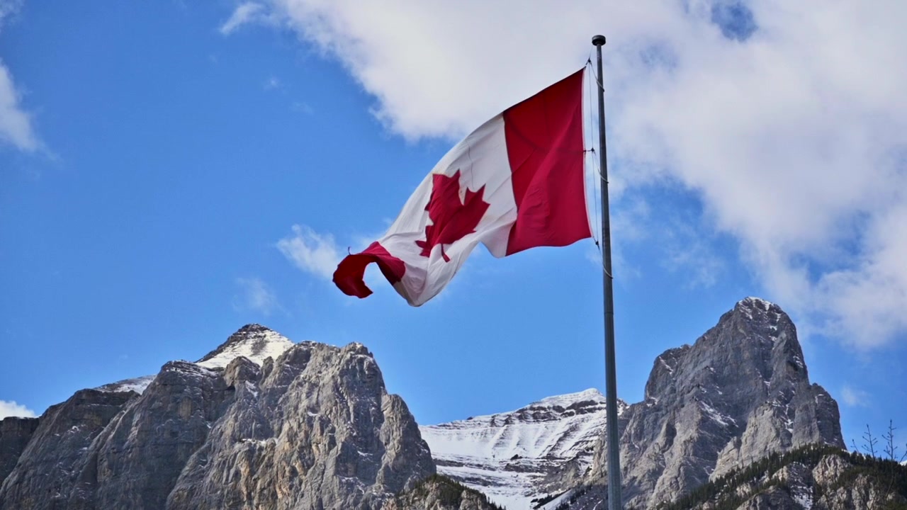 Bandiera canadese che sventola con le Montagne Rocciose canadesi sullo sfondo.