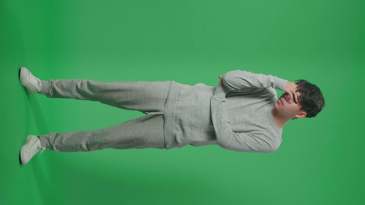 cuerpo lleno de hombre asiático con dolor de cabeza mientras está de pie frente al fondo de la pantalla verde