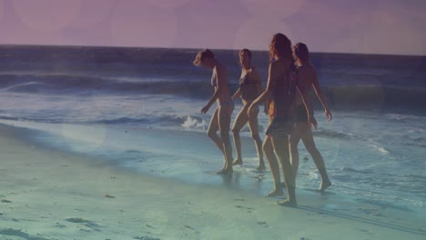 Animation-of-glowing-lights-over-group-of-diverse-female-friends-by-the-sea