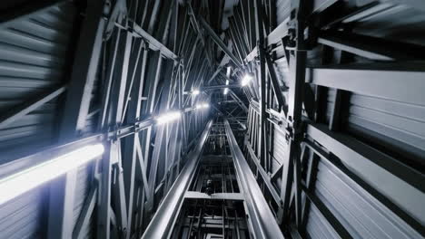 looking up a modern elevator shaft with metal structures and lights