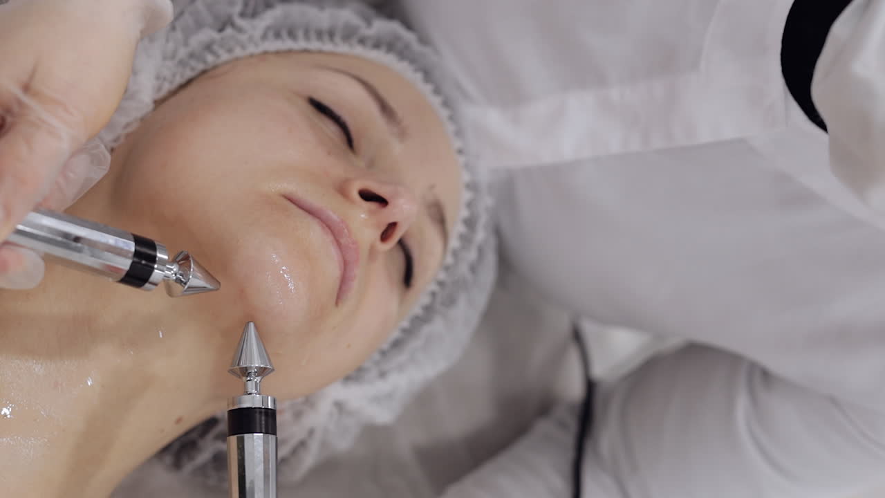 미용학자 의사는 스파 살롱에서 전기 충동을 사용하여 여성 마이크로 전류 얼굴 치료를합니다.