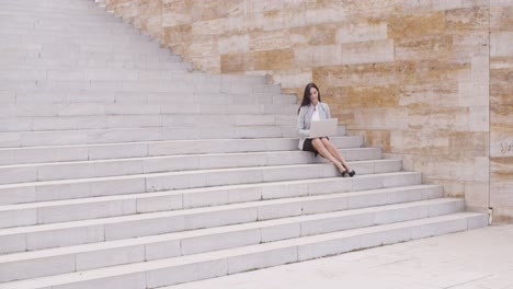 Pretty-young-worker-sitting-on-steps-with-laptop