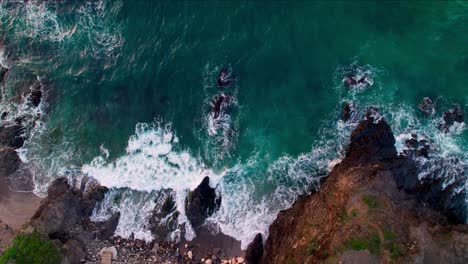 top down aerial view from above of ocean waves crashing and foaming on empty tropical beach with stones