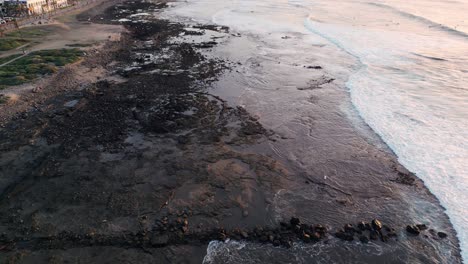 Aerial-view-of-the-waves-crashing-on-the-rocky-shoreline-at-sunset