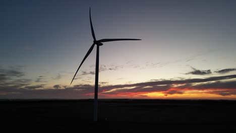 The-silhouette-of-a-wind-turbine-spinning-during-an-orange-sunset-on-the-horizon