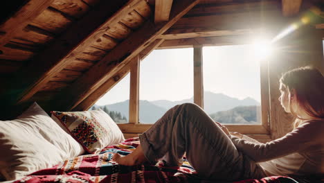 young woman gazing at mountains from a rustic cabin window