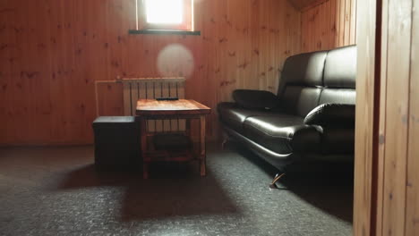 wood paneled room interior featuring leather couch and rustic wood table beneath bright window glow, framed by open doorway and natural grain textures for warm cozy inviting atmosphere