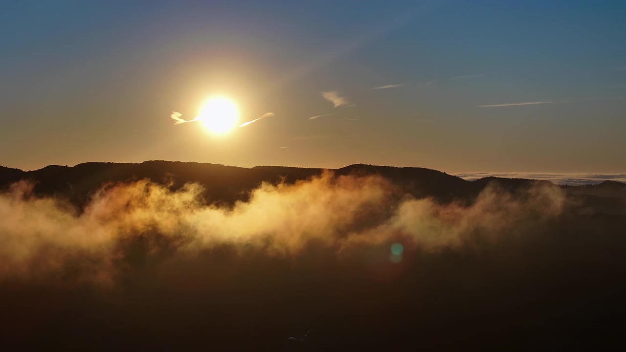 Dichte gouden mistbank onder de opkomende zon en bergkam.
