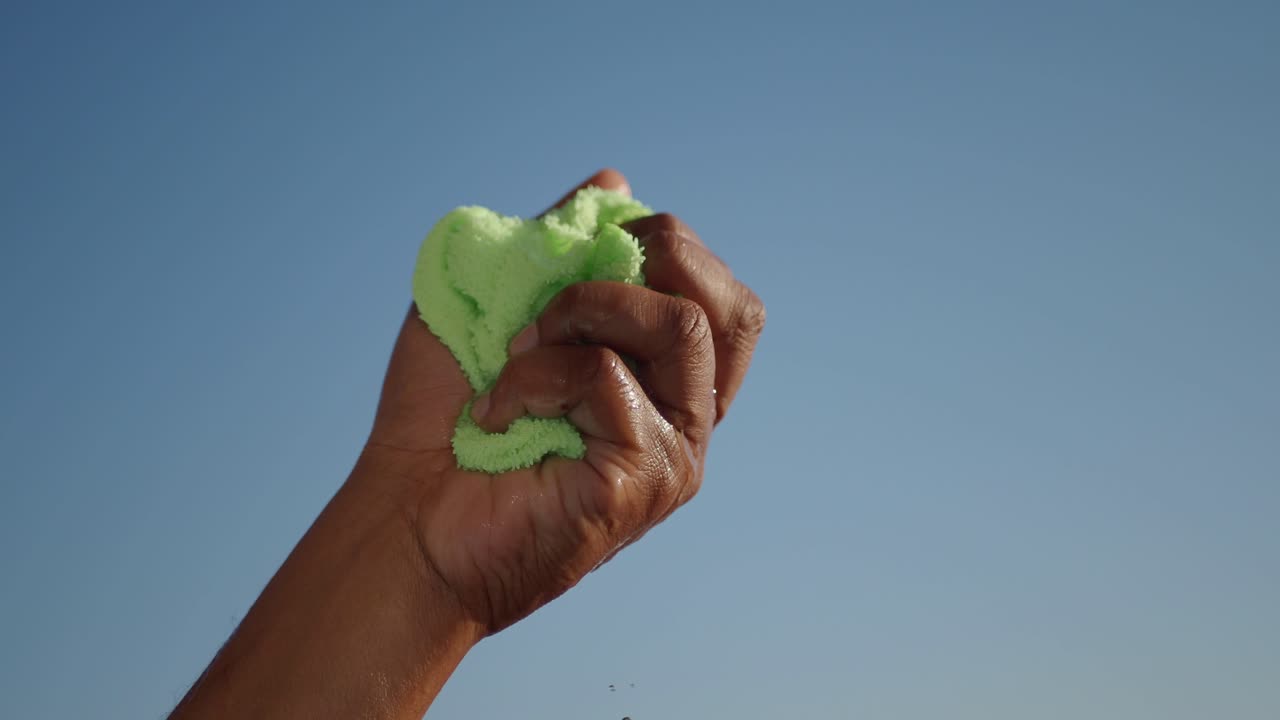 la mano apretando una esponja verde con goteo de agua