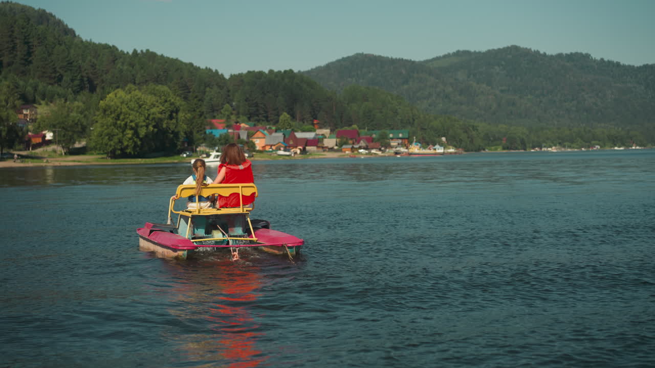 madre joven y niño pequeño en catamarán en el lago. vacaciones familiares en el embalse en cámara lenta. entretenimiento activo en un cálido día de verano vista trasera