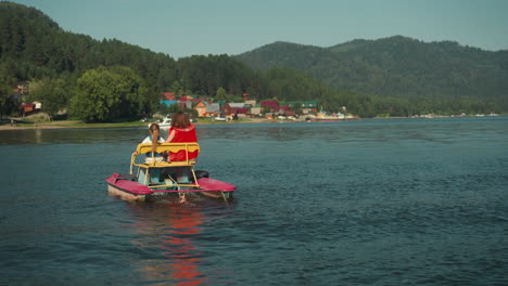 young mother and little child ride catamaran on lake. family vacation at reservoir slow motion. active entertainment on warm summer day backside view