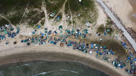 Traditional-Vietnamese-coracle-boats-stored-on-the-beach,-surfers-enter