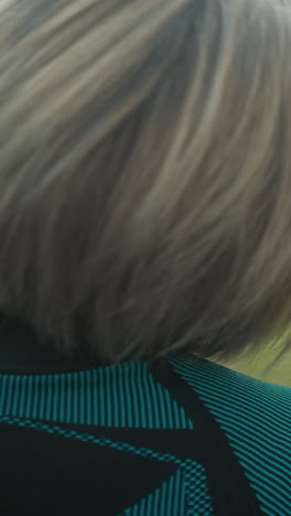 vista trasera de la mujer en traje negro y verde, ojos cerrados, inclinando la cabeza lentamente de derecha a izquierda, estirando y relajando los músculos del cuello al aire libre en un campo tranquilo de hierba bajo un cielo nublado