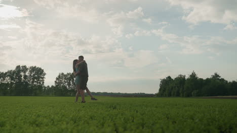 friends running across lush green field toward each other then embracing in joyful hug as man turns partner around with wide smile under bright sky