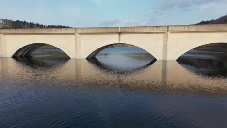 Aerial-drone-flight-over-Ladybower-Reservoir-and-under-an-archway-of-the-bridge-in-Derwent-Vally-in-the-Peak-District