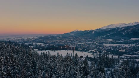 Stunning-Drone-Winter-Aerial-Shot-Pine-Trees-Moving-onto-Hotel-Bachleda-Poland-during-golden-hour