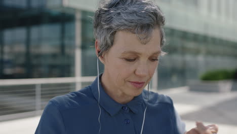 portrait of mature independent business woman listening to music using earphones wearing backpack in city