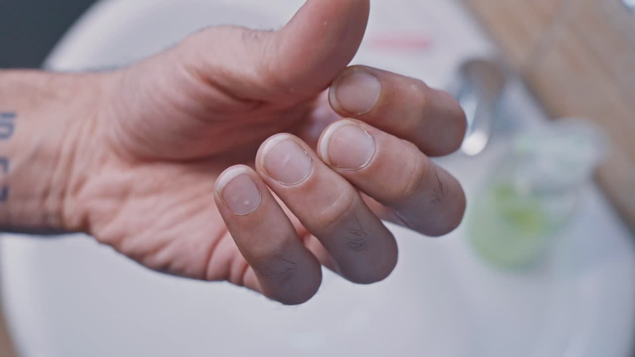 Detailed close-up view of a man's hand applying nourishing oil to his cuticles for a manicure, promoting healthy nail growth