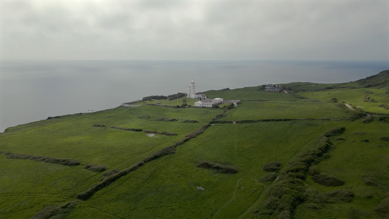Forward drone shot flying over green cliffs toward St. Catherine’s Lighthouse