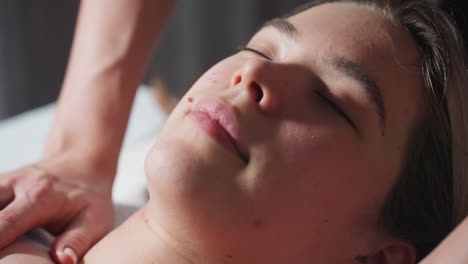 close up view of light-skinned young woman lying with closed eyes while enjoying gentle massage session, showing peaceful expression and calm atmosphere in indoor wellness spa environment