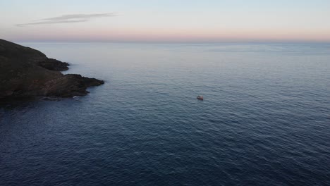 aerial drone view of cornish coast at dusk, featuring a small fishing boat and enchanting scenery