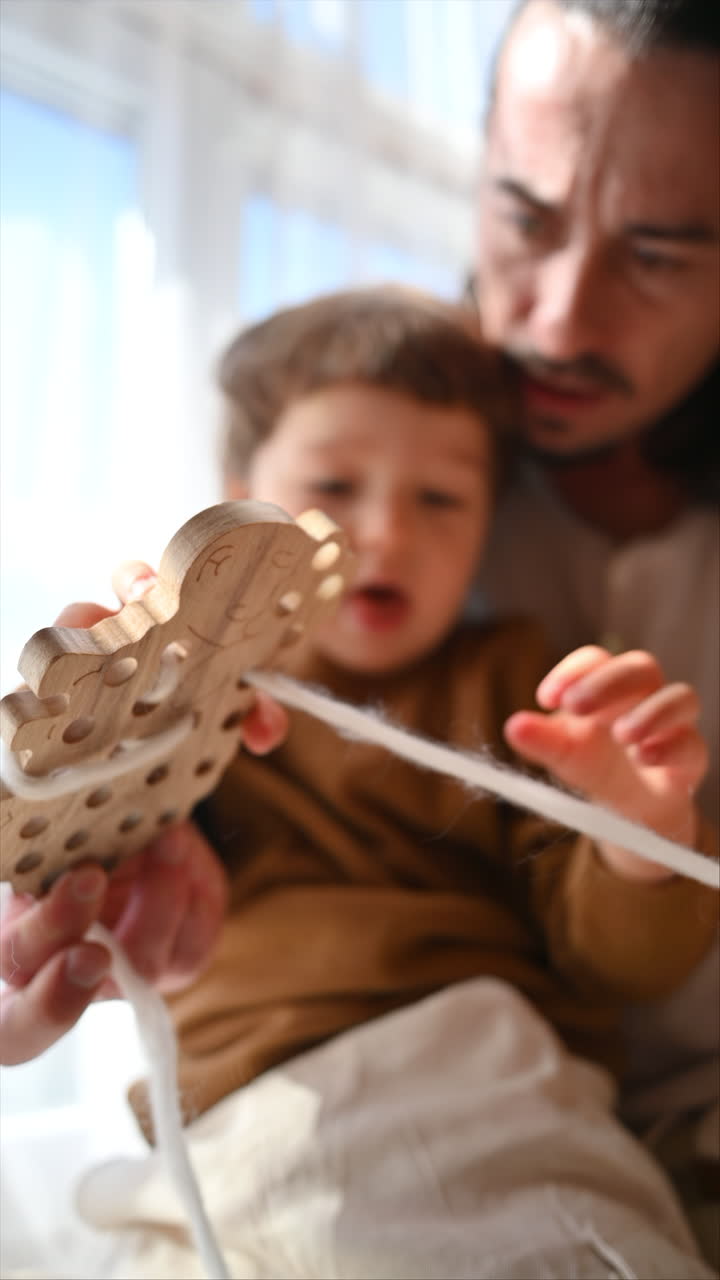 Father playing with his son with ecological wooden toys near the window. Vertical