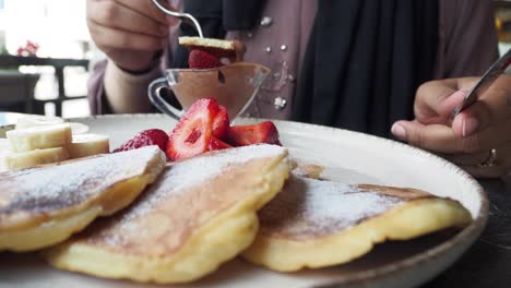 woman eating pancakes with strawberries, bananas, and chocolate sauce