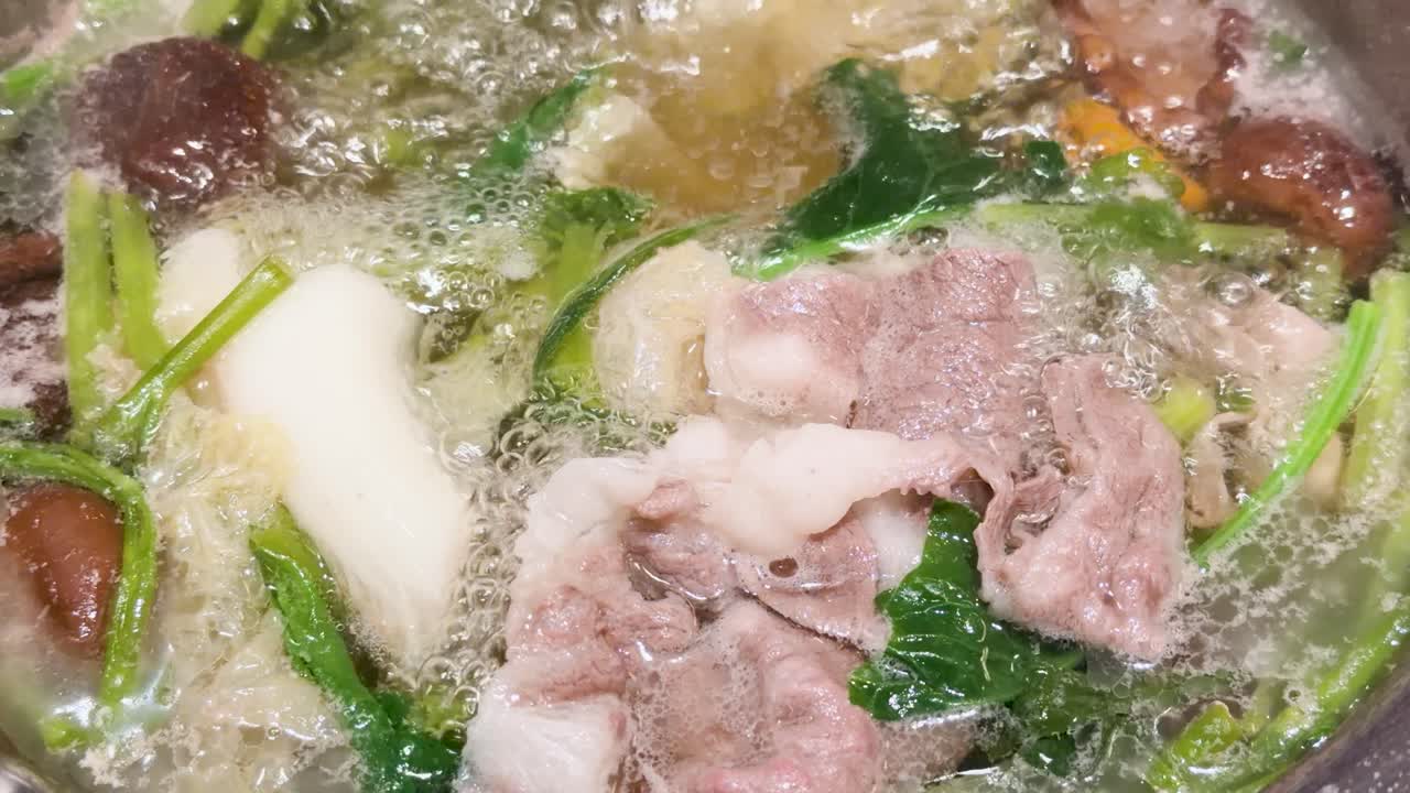 Close-up of assorted meats and vegetables simmering in bubbling hotpot broth, overhead view