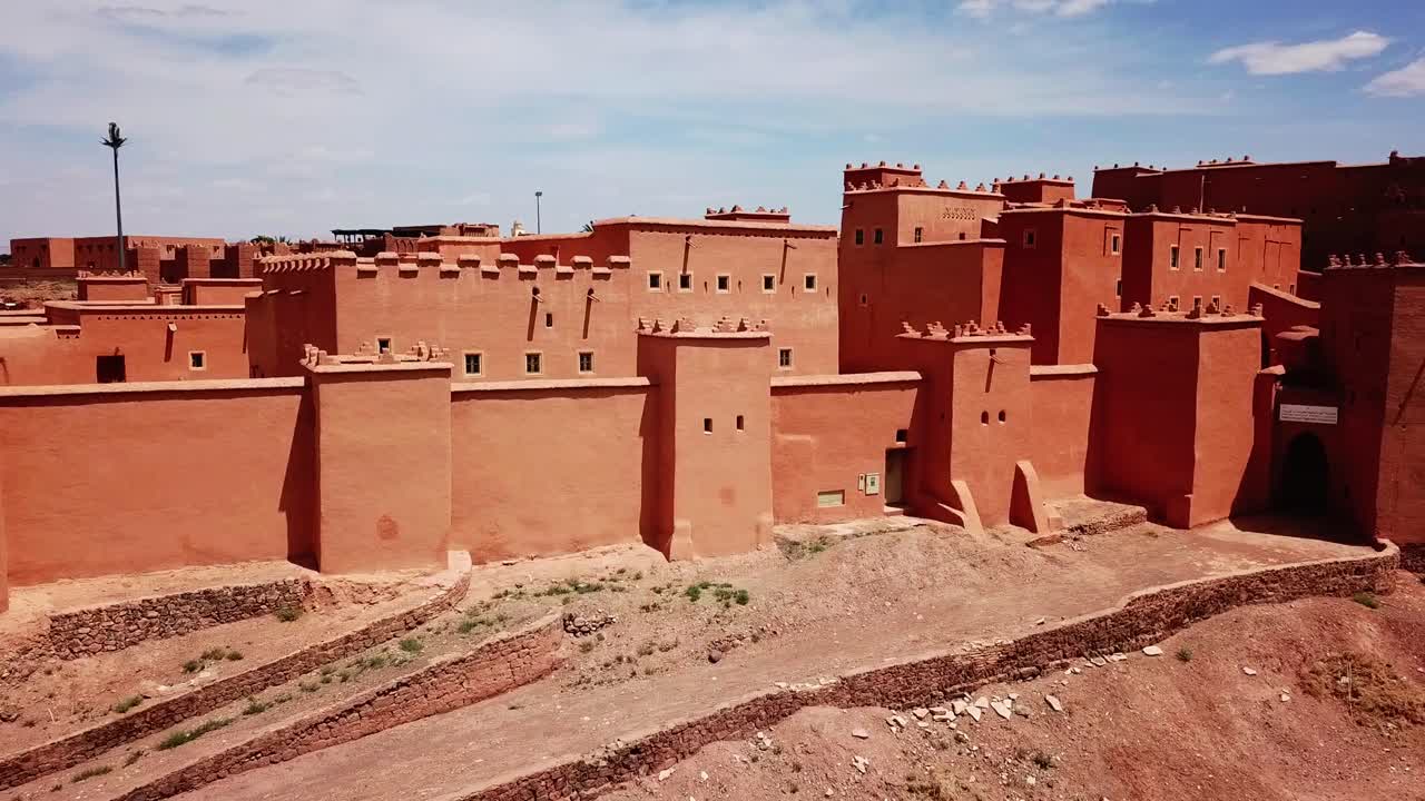 Vista di mura fortificate e torri di una kasbah marocchina a Ouarzazate, che mostra l'architettura difensiva tradizionale in un ambiente desertico. Ideale per immagini di patrimonio e storiche.